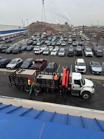 Rigging trucks staged below a commercial roof for a rooftop unit lift
